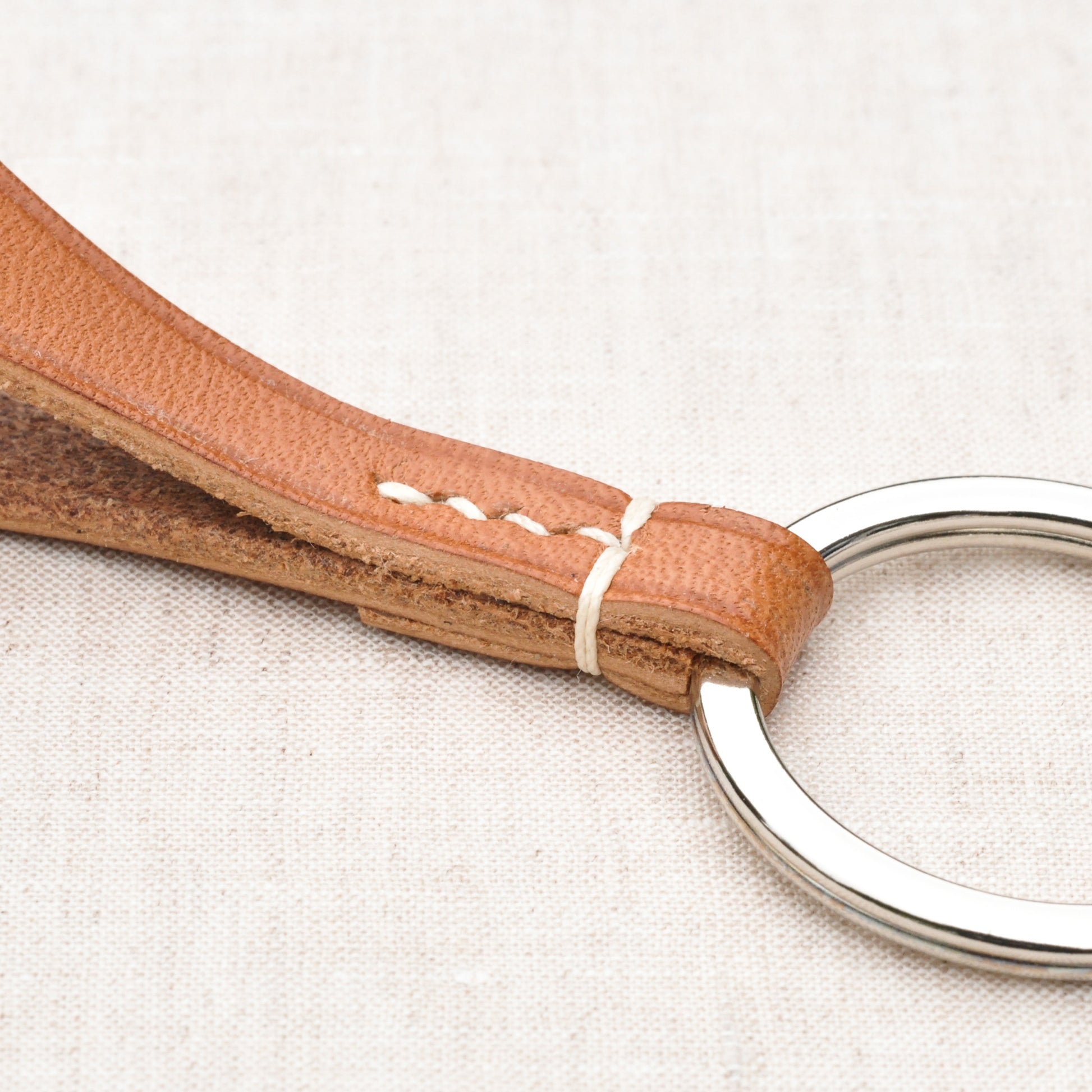 Vue en détail d'un porte-clés en cuir naturel et de son assemblage au point sellier présentant deux points à cheval.